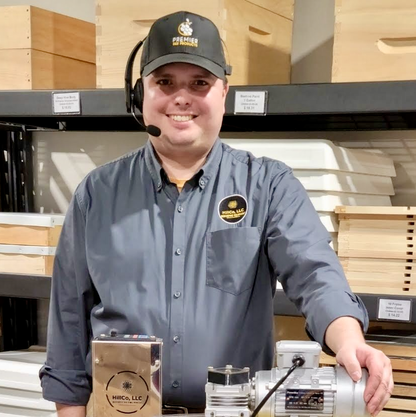 Person wearing a branded shirt and cap, standing with industrial equipment in a warehouse setting.