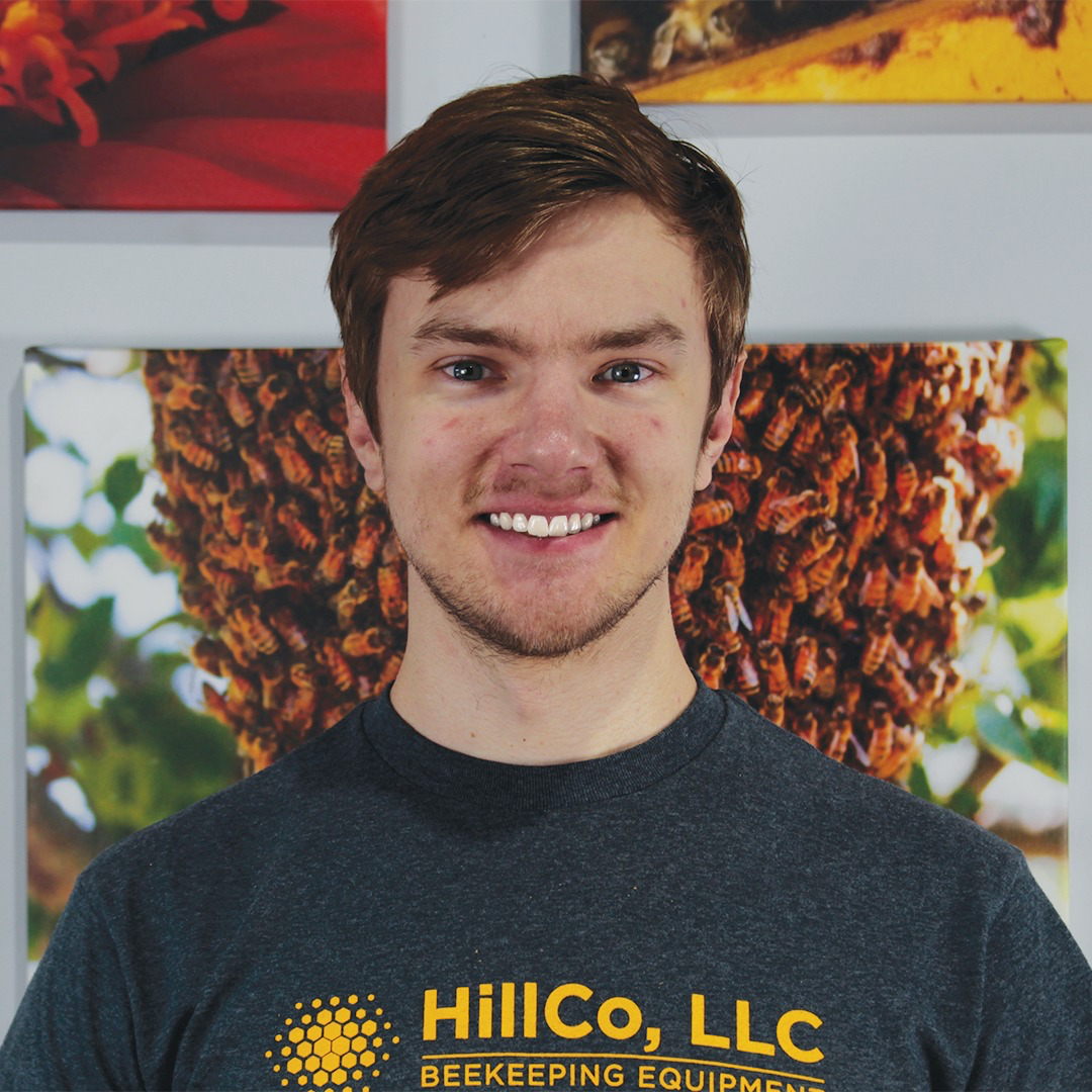 Person wearing a HillCo, LLC beekeeping equipment shirt in front of bee-themed posters.